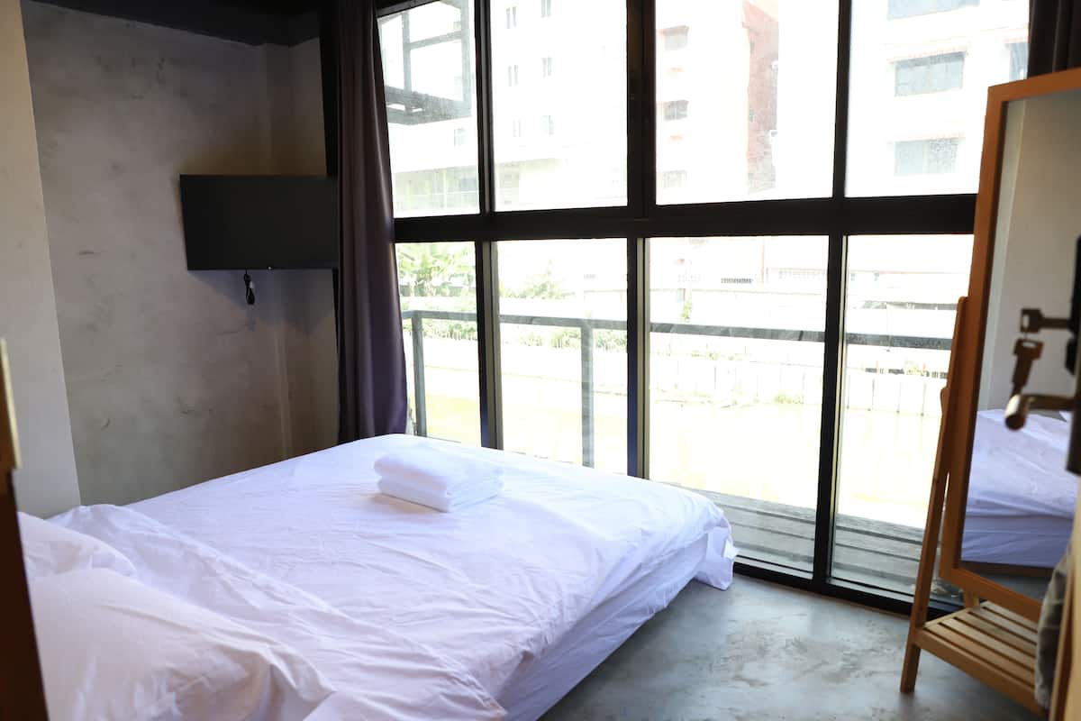 Une chambre d’hôtel équipée d’un lit, d’un téléviseur fixé au mur et de grandes fenêtres donnant sur l’extérieur.
