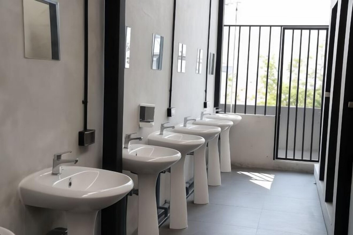 A row of white sinks with a modern design, a mirror, and a black metal gate in a well-lit bathroom.