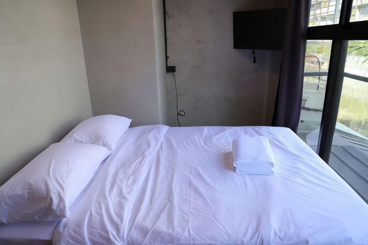 Une chambre d’hôtel avec un lit, du linge de lit blanc, un téléviseur à écran plat fixé au mur et une fenêtre donnant sur l’extérieur.