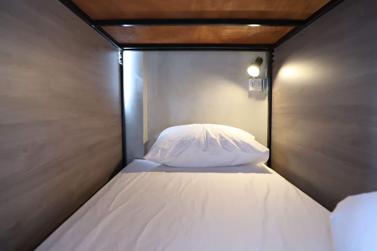 Une petite chambre avec un lit simple, un plafond en bois et un luminaire fixé au mur.