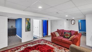 Amplia sala de estar con alfombra roja, un sofá rojo y una cocina visible a través de una puerta abierta.