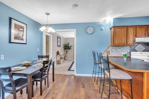 Un comedor con una mesa y sillas de madera, una cocina con armarios de madera y un reloj en la pared.