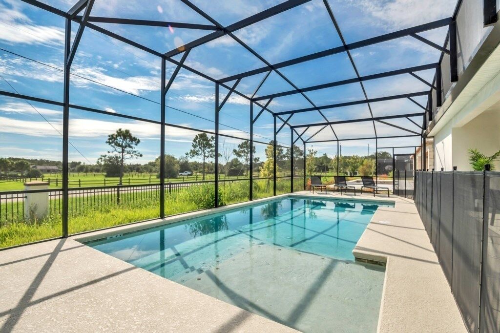 A covered outdoor swimming pool with a view of a green landscape and a clear sky.