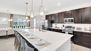 A modern kitchen with dark wooden cabinets, stainless steel appliances, and a central island with bar stools. - The Ultimate New 15 Bedroom Vernada Villa by RedAwning (Kissimmee)