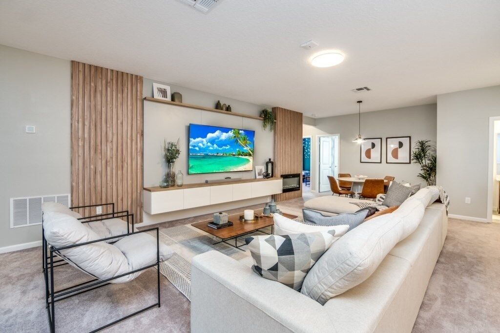 A modern living room with a large flat-screen TV, a sofa, a coffee table, and a dining area with chairs.