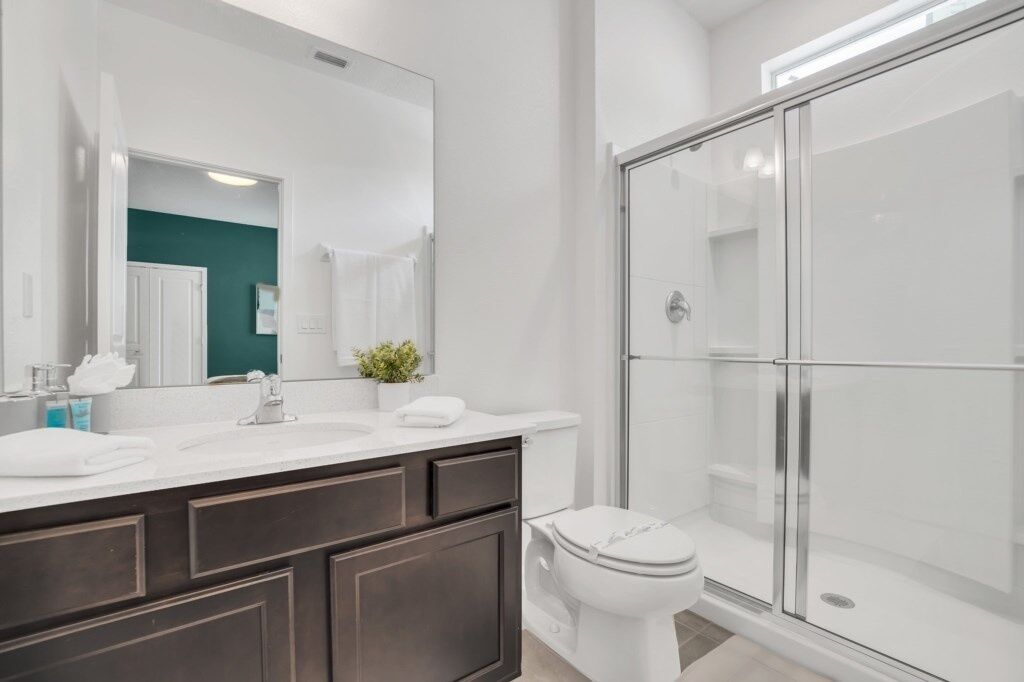 A modern bathroom with a white sink, dark wooden vanity, a white toilet, and a glass-enclosed shower.