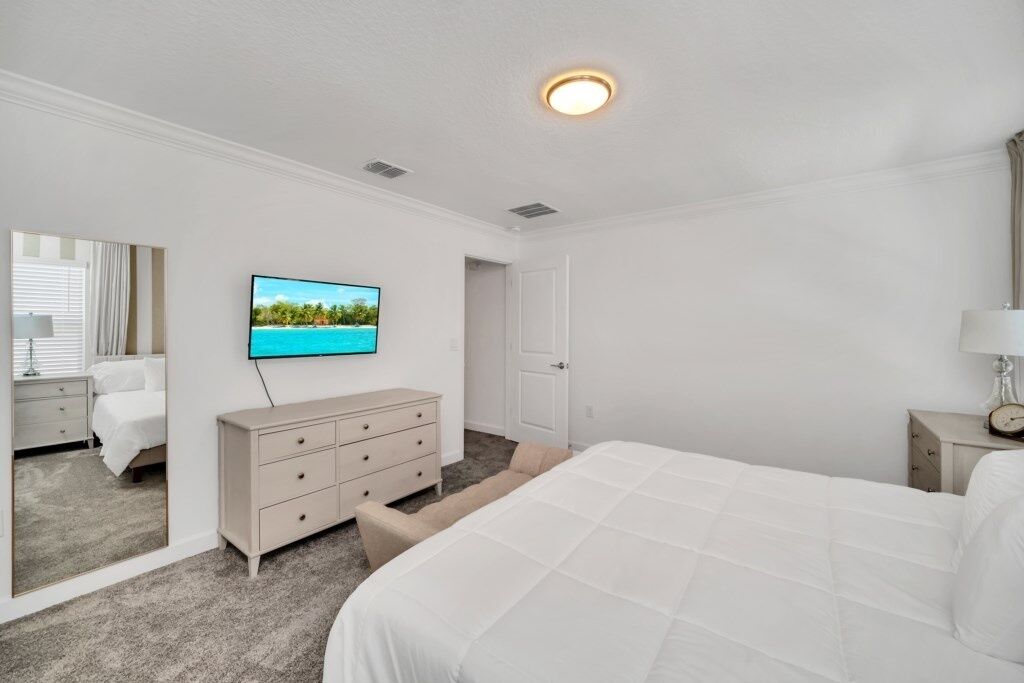 A hotel room with a large bed, a dresser, a television mounted on the wall, and a door.