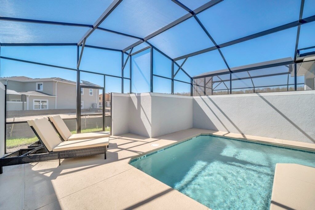 An indoor swimming pool with a glass enclosure, lounge chairs, and a view of the surrounding neighborhood.