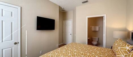 A bedroom with a large bed, a television mounted on the wall, a door, and a bathroom visible through an open door.