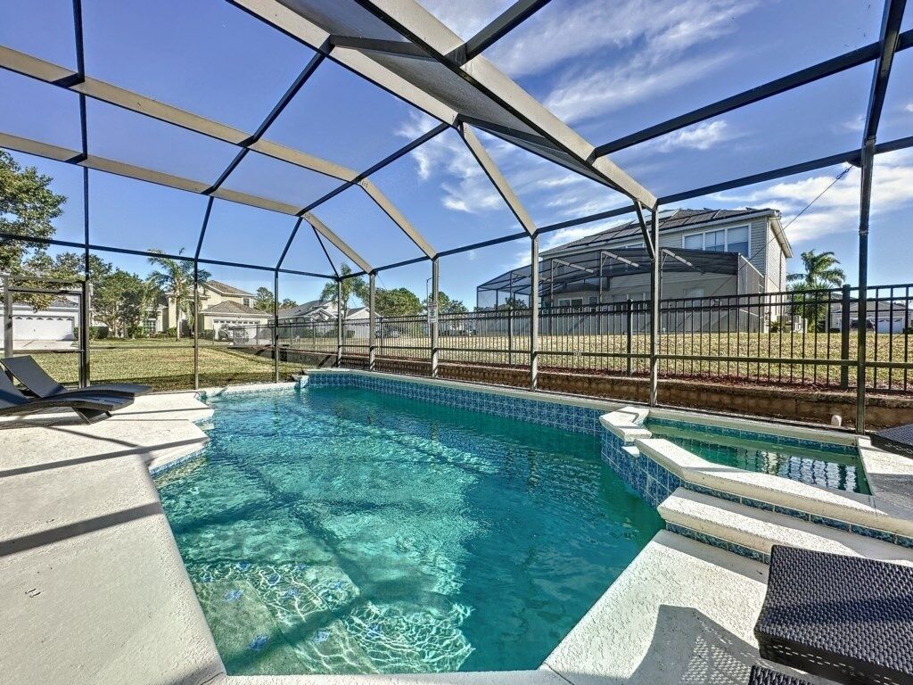 A swimming pool with a clear blue water, surrounded by a covered area with a metal frame and a fence.
