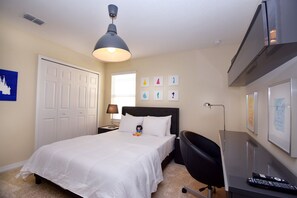 Quarto de hotel com cama, escrivaninha, cadeira, abajur e obras de arte nas paredes.