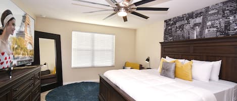 A bedroom with a bed, a ceiling fan, a window with blinds, a dresser, and a cityscape wall art.