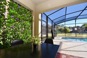 A covered outdoor area with a pool, a table with chairs, and a wall with climbing plants. - 1705vp 4 Bedroom Home by RedAwning (Kissimmee)