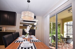 A dining area with a table set for four, a chandelier, and a view of a garden through a sliding glass door. - 1705vp 4 Bedroom Home by RedAwning (Kissimmee)