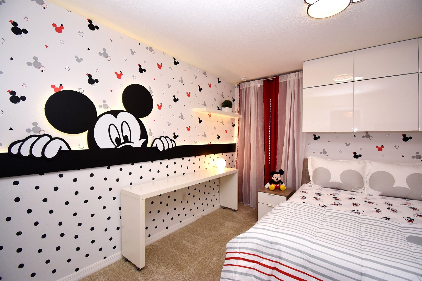 A bedroom with Mickey Mouse wall decals, a bed with striped bedding, a desk, and a nightstand.