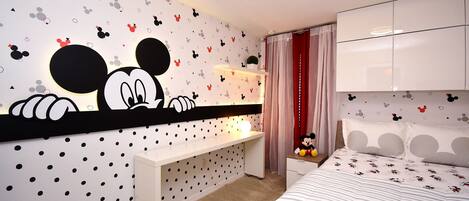 A bedroom with Mickey Mouse wall decals, a bed with striped bedding, a desk, and a nightstand.
