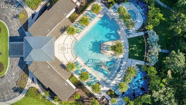 Vista aérea de un complejo turístico con piscina central, zonas de descanso y palmeras.