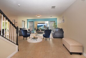 A spacious living room with a staircase, a flat-screen TV, and a large window with blinds. - 1705vp 4 Bedroom Home by RedAwning (Kissimmee)