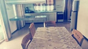 Ein Essbereich mit Tisch und Stühlen, im Hintergrund eine Küche und ein Kühlschrank.