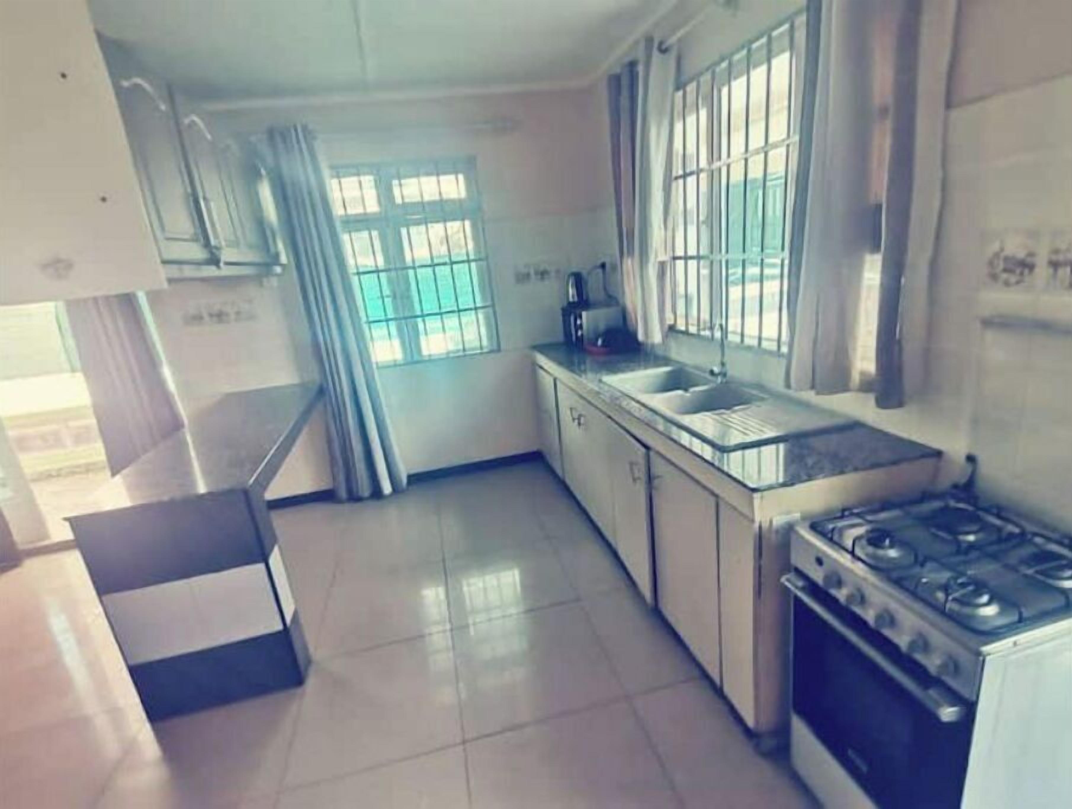 A kitchen with a gas stove, a sink, and a window with bars.