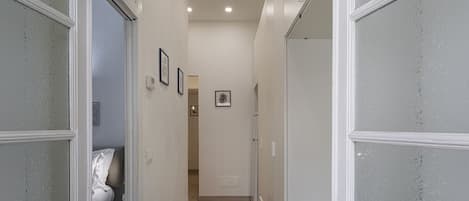 Un couloir étroit, avec un lit sur la gauche et une porte sur la droite.