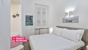 Ein Schlafzimmer mit einem Bett, einem Vorhangfenster, einem Bild und einer Wandleuchte.