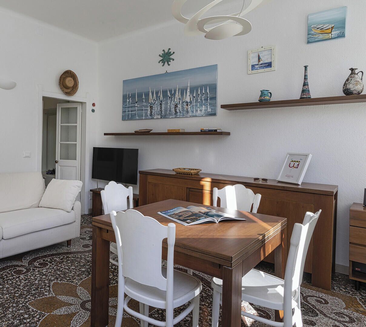 Ein modernes Wohnzimmer mit einem weißen Sofa, einem Holzespeisetisch mit weißen Stühlen, einem Fernseher und Kunstwerken an den Wänden.
