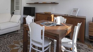 Ein modernes Wohnzimmer mit einem weißen Sofa, einem Holzespeisetisch mit weißen Stühlen, einem Fernseher und Kunstwerken an den Wänden.