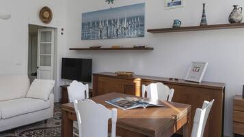 Ein modernes Wohnzimmer mit einem weißen Sofa, einem Holzespeisetisch mit weißen Stühlen, einem Fernseher und Kunstwerken an den Wänden.