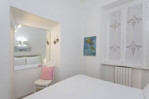 Ein Schlafzimmer mit einem Bett, einem Sessel, einem Spiegel, Wandbildern und einem Fenster mit Dekoration.