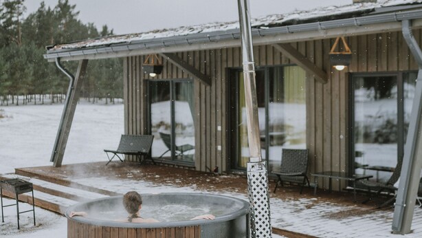 Puinen poreallas terassilla, jonka yhteydessä on sauna. Porealtaan ympärillä on ulkokalusteita ja lumipeitteinen maisema.