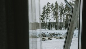 Näkymä rakennuksen sisältä, josta avautuu lumisen metsän ja puisen terassin maisema.