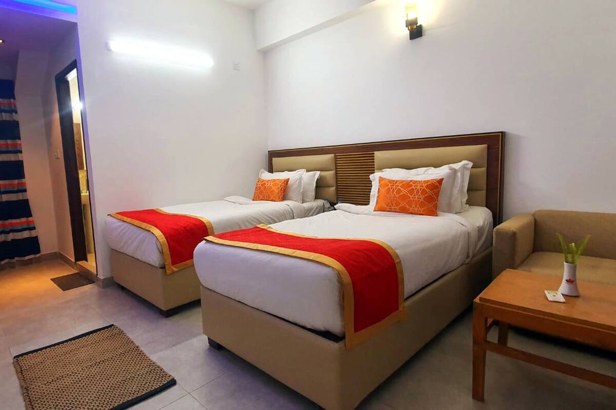 Ein Hotelzimmer mit zwei Betten, einem Schlafsofa, einem kleinen Tisch und einem an der Wand befestigten Fernseher.
