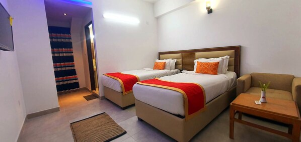 A hotel room with two beds, a sofa, a small table, and a wall-mounted TV.