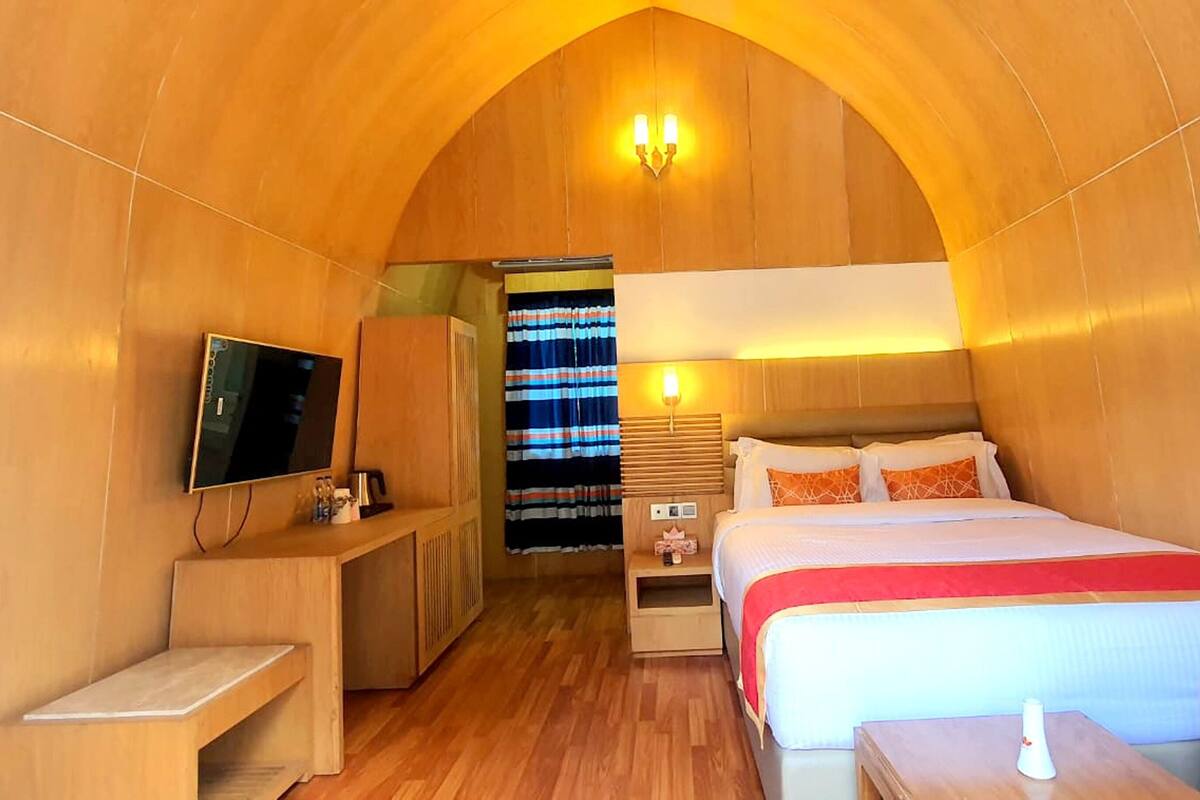 Ein Hotelzimmer mit Holzvertäfelung, einem Bett mit rot-weißer Bettdecke, einem Fernseher auf einem Holztisch und einem Fenster mit gestreiften Vorhängen.