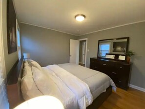 A bedroom with a bed, dresser, and a door leading to another room. - Spacious 3BR Home w Parking. Perfect for Families & Longer Stays (Chicago)