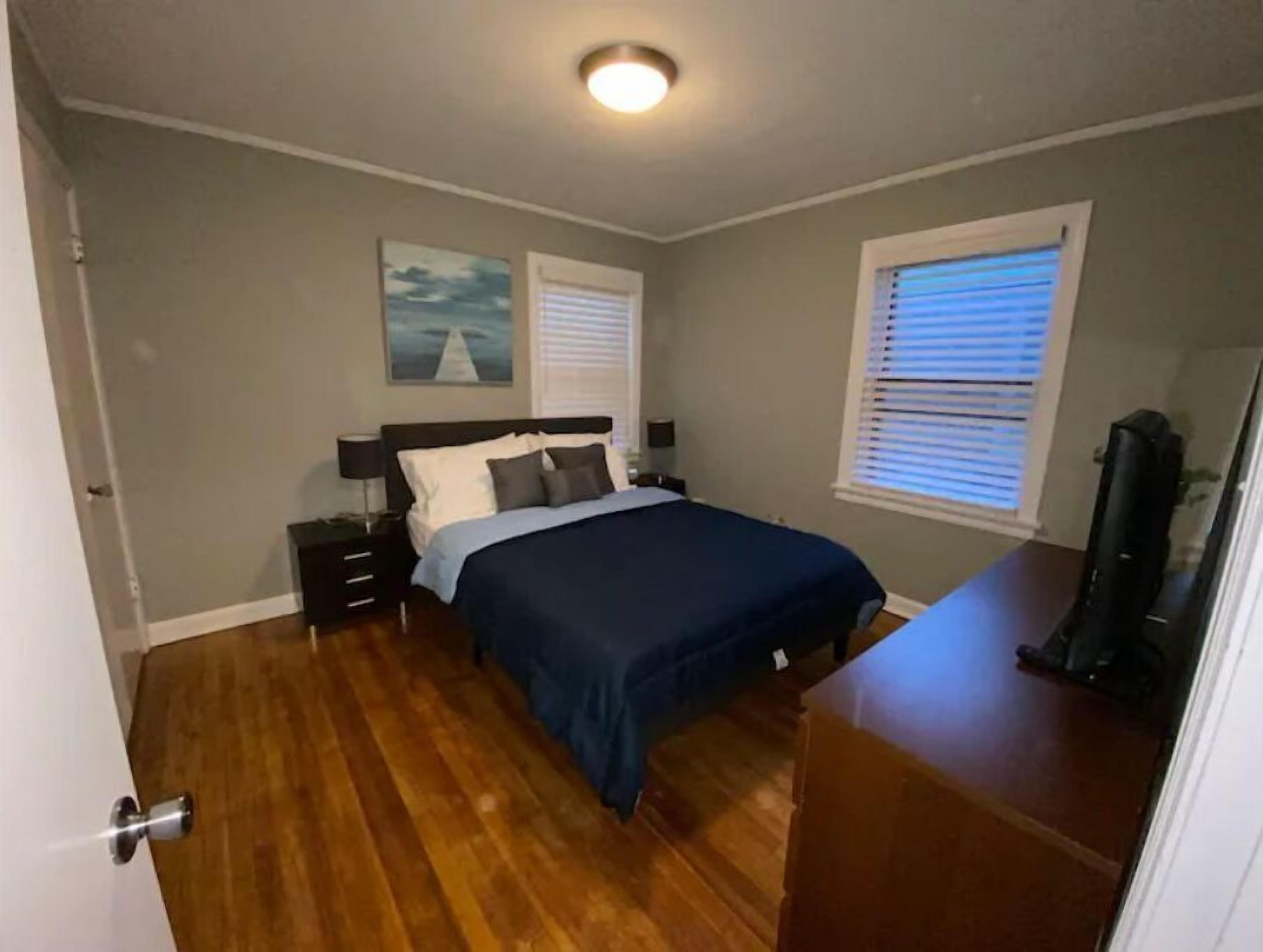 A bedroom with a bed, nightstands, a dresser, a window with blinds, and a ceiling light.