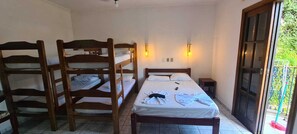 Quarto com beliches, uma cama de solteiro, uma mesa pequena e janela com vista para o verde.
