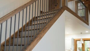 A wooden staircase with metal railings leading to an upper floor. A table with a lamp and decorative items is placed on the lower landing. - An Oasis indeed in Amish Country (Millersburg)