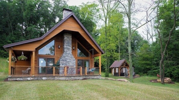 A log cabin with a stone fireplace, large windows, and a porch with chairs. - An Oasis indeed in Amish Country (Millersburg)