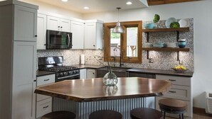 A modern kitchen with white cabinets, a central island with stools, a microwave, stove, and a hanging light fixture. - An Oasis indeed in Amish Country (Millersburg)