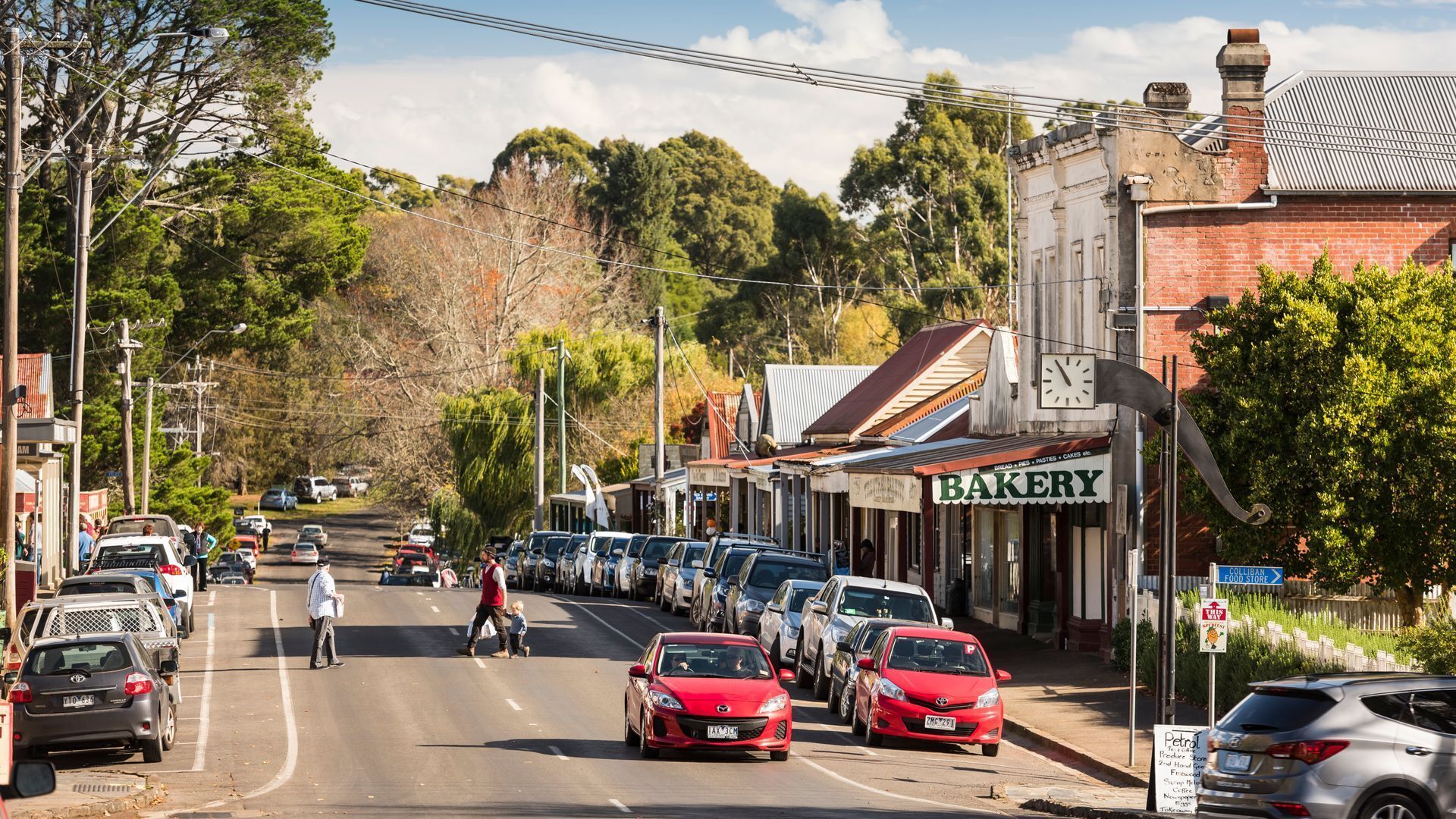 A street lined with parked cars, a bakery, and a clock on a building.