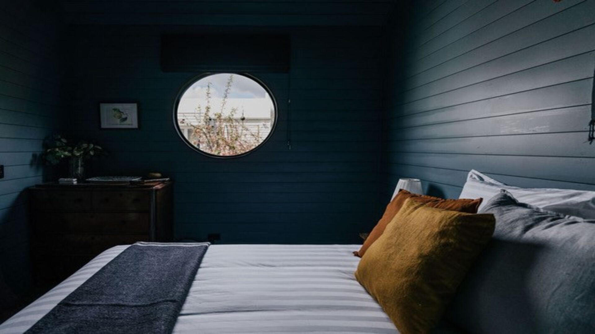 Een slaapkamer met een bed, nachtkastje, raam en een kledingkast.