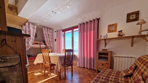 Une pièce chaleureuse avec un plancher en bois, une table à manger avec des chaises, un canapé et une fenêtre avec des rideaux.