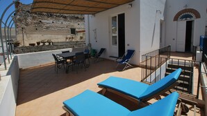 A sunlit outdoor patio with lounge chairs, a table, and a covered seating area. - Casa Al Mar Canneto Via Mazzini (Lipari)