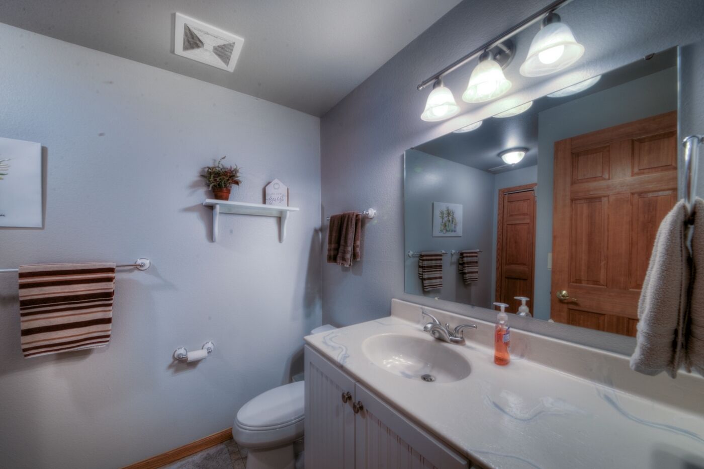 Een badkamer met een wastafel, toilet en spiegel. Handdoekrek met handdoeken en een klein plankje met een plantje.
