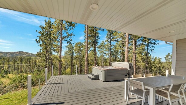 Eine Terrasse mit Whirlpool, Tisch und Stühlen, umgeben von Wald und Bergblick.