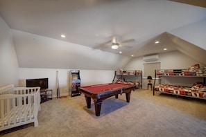 Una habitación con mesa de billar, literas, televisor y máquina de pinball.