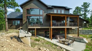 Een tweelaags huis met een balkon, een terras met tuinmeubilair en een stenen steunmuur.