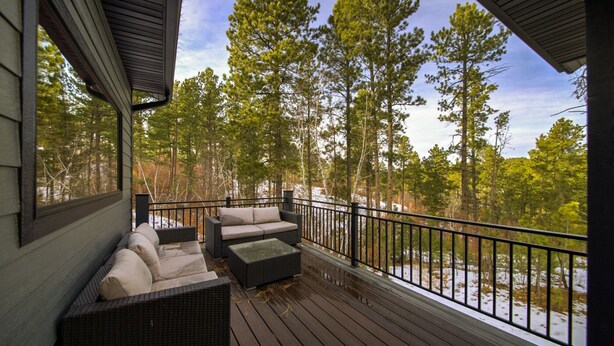 Una terraza techada con mobiliario exterior y barandilla con vista a un bosque.